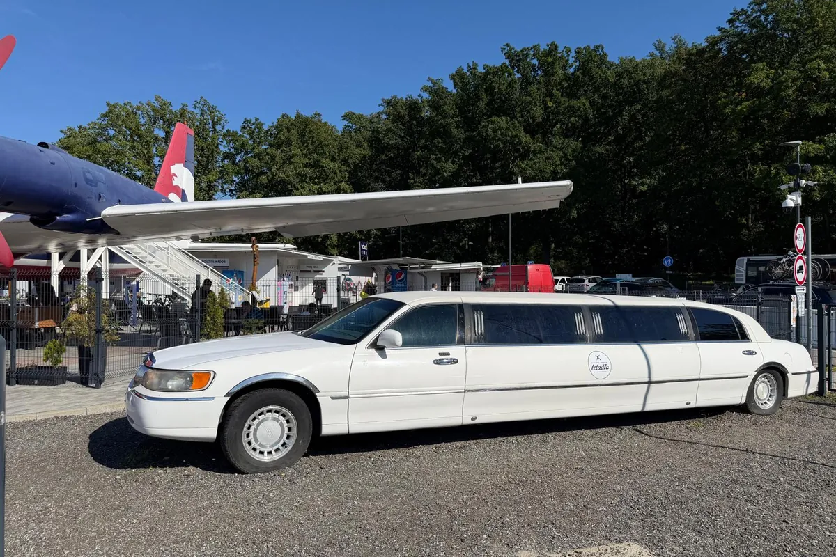 Bílá prodloužená limuzína Lincoln Town Car zaparkovaná pod křídlem letadla