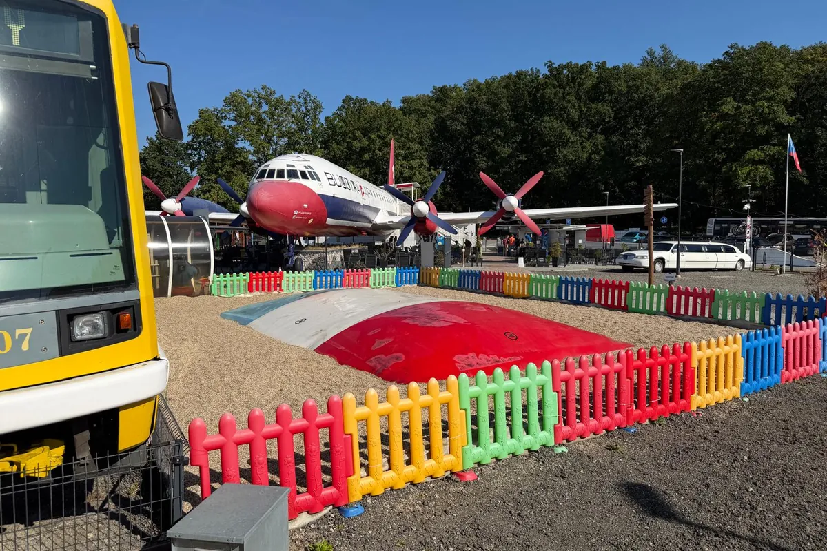 Velká nafukovací trampolína ohrazená barevným plůtkem, mezi tramvají a letounem